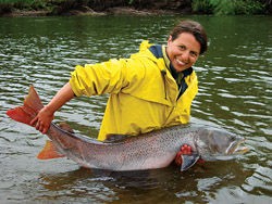 A woman holding a salmonid in a river